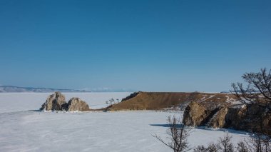 Donmuş gölün uçsuz bucaksızlığında, bitki örtüsünden yoksun, iki başlı sıra dışı bir kaya yükselir. Dik kayalık yamaçlar. Buz tamamen karla kaplı. Açık mavi gökyüzü. Baykal.