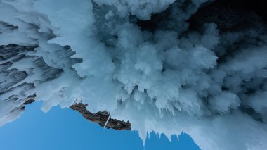 Buz sarkıtları kayadaki bir mağaranın tavanında asılı. Açık mavi gökyüzüne karşı tuhaf, alışılmadık bir buz şekli. Yakın plan. Baykal.