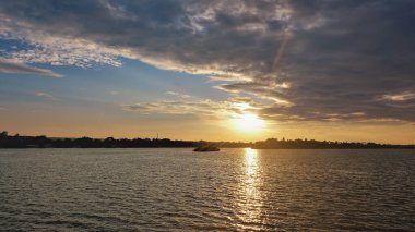 Nehrin üzerinde gün batımı. Gökyüzünde mor bulutlar var. Güneş ışınları ufkun üstündeki gökyüzünü altın renklerle boyar. Sudaki güneşli yol. Zambesi. Zimbabwe.