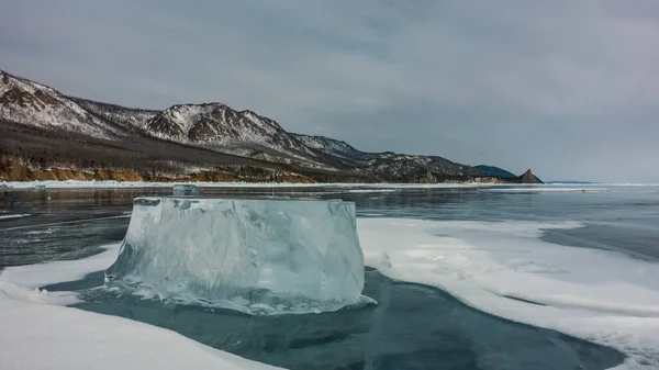 凍った湖の上には大きな輝く氷の流れが広がっています 接近中だ テクスチャ 少し雪 表面の亀裂 雪の空の背景に山の範囲をかぶった バイカル — ストック写真