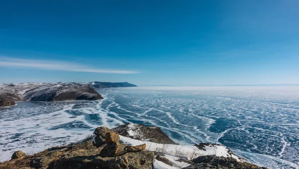 冰封湖中的蓝色冰层上可见雪纹 岩岸没有植被 风景如画的石头在前景中 晴朗的蓝天 冬日贝加尔湖 — 图库照片