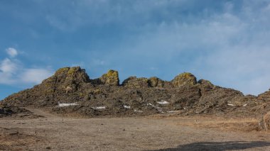 Mavi bir gökyüzünün arka planında bitki örtüsünden yoksun tuhaf bir dağ sırası. Taşlarda çatlaklar, sarı zambaklar. Yerde biraz kar var. Kış güneşli bir gün. Baykal..