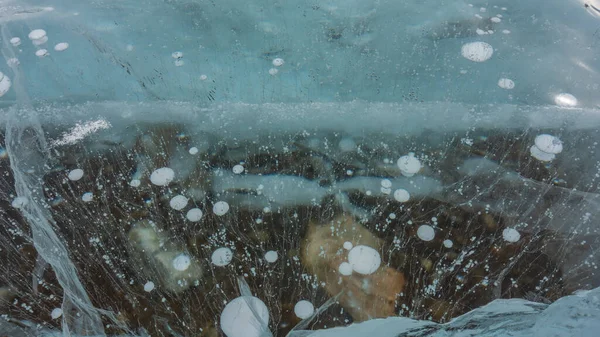 透明な氷 クローズアップ 表面に亀裂 深部には 凍結したメタンガスの泡があります 下に横たわる石が見える フルスクリーン バイカル湖 — ストック写真