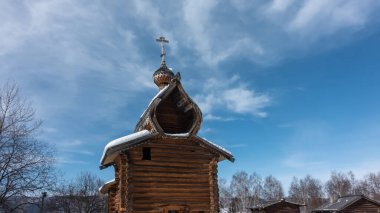 Eski kilise boyanmamış kütüklerden inşa edildi. Mavi gökyüzüne karşı kubbeler ve haçlar. Çatıda kar var. Sibirya.