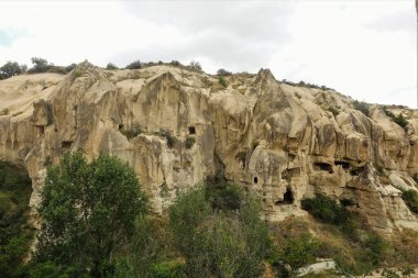 Katlanmış yamaçları ve keskin tepeleri olan Cappadocia 'nın inanılmaz kayaları. Taşların üzerine antik mağaralar oyulmuş. Vadideki yeşil bitki örtüsü. Türkiye