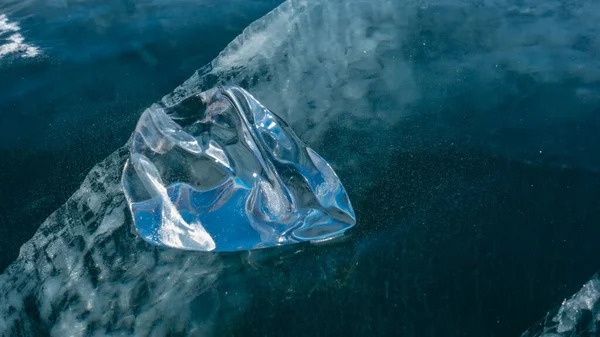 Shiny shard of ice, close-up, detail. Glare of the sun on the edges. A crack can be seen going into the depths of the frozen lake. Baikal