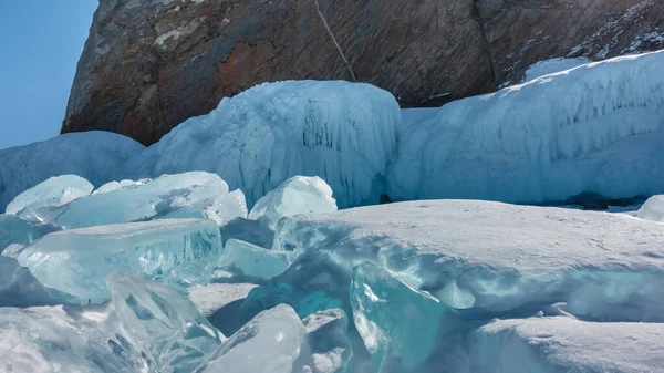 花岗岩的底部被冰柱覆盖着 旁边是一块透明的绿松石浮冰 边缘闪烁着光芒 表面白雪 贝加尔湖 — 图库照片