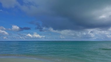 Aquamarine okyanusu sakindir. Dalgalar kumlu sahilde sıçrıyor. Gök mavimsi bulutlar var. Birkaç beyaz bulut ve bir büyük yağmur bulutu. Maldivler yazı