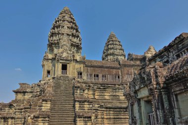 Ünlü Angkor 'daki antik bir tapınağın parçası. Harap olmuş bir taş merdiven, galerisi olan bir terasa çıkıyor. Açık mavi gökyüzüne karşı yüksek oymalı kuleler. Kamboçya
