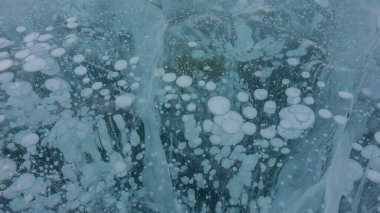 Turkuaz buz yüzeyi. Yakın plan. Tam kare. Çapraz çatlaklar, donmuş metan gazı kabarcıkları görülebilir. Baykal Gölü