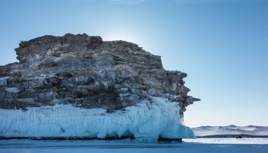 Donmuş Baykal Gölü 'nde tuhaf hatları olan granit bir kaya yükseliyor. Taşlarda çatlaklar var. Taban buz saçaklarıyla kaplı. Uzakta karla kaplı dağlar. Mavi gökyüzü. Kış günü
