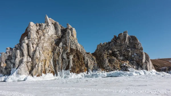 植生のない2つの頭の岩は 凍結した湖の上に上昇する 岩の上に亀裂 崖の底につららの厚い層 氷の上の雪 真っ青な空 バイカル — ストック写真