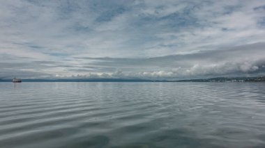 Pasifik Okyanusu 'nun sularında hafif bir dalgalanma var. Uzakta, yalnız bir gemi ve kıyıda bir şehir görebilirsiniz. Mavi gökyüzünde pitoresk bulutlar var. Kamçatka.