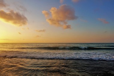 Golden dawn in Mexico. Orange glow over the horizon. There are pinkish clouds in the blue sky. Surf waves are foaming on the sandy beach. The Caribbean Sea. clipart