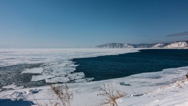 Dondurucu olmayan bir nehir donmuş bir gölden akar. Mavi su ve beyaz buz. Buz kütleleri yüzeyde yüzer. Kıyıda kar ve kuru çimenler. Gök mavisi gökyüzüne karşı dağlar. Baikal. Angara.
