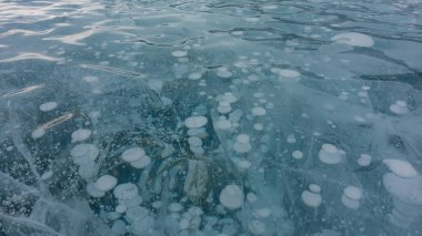 Şeffaf soluk mavi buz. Yakın plan. Detaylı. Tam ekran. Parlak dalgalı yüzey. Çatlaklar ve donmuş metan kabarcıkları görülebilir. Baykal Gölü