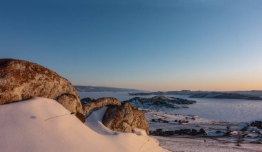 Sibirya 'da sabah altın saati. Donmuş bir gölün buzunda parıltı. Sahilde bir köy. Ön planda pitoresk kayalar var. Kar güneşin pembe ışınlarında parıldıyor. Baykal.