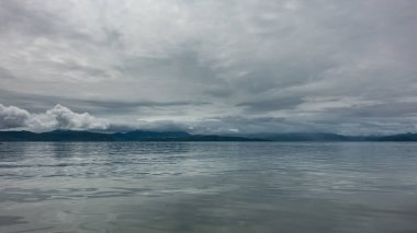 Bulutlu bir gökyüzünün altındaki okyanus. Parlak bir yüzeyde yansıma. Uzakta bir dağ sırası görebilirsiniz. Tepeleri bulutların arasında gizlidir. Pastel gözlük. Petropavlovsk-Kamçatsky. 