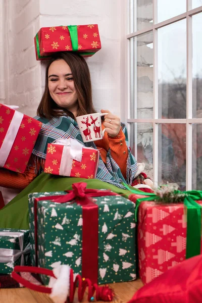 A beautiful girl in an orange jacket opens a New Year\'s gift in a box with tape. Christmas Day, New Year\'s Eve