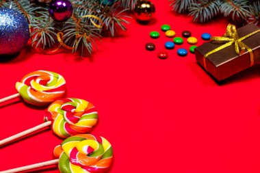 Kırmızı zemin üzerinde çok renkli lolipoplar ve şekerler Noel süsü, hediyeler ve ladin dallarıyla. Bir pastane bayrağı.