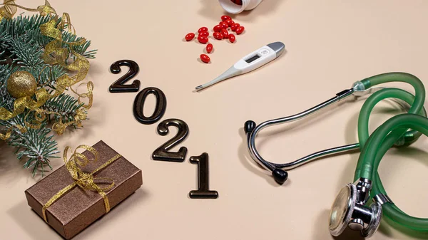 New Year\'s card on medical subjects: figures 2021, phonendoscope, tablet with spruce branch on a beige background. New Year 2021 medicine.