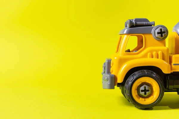 Construction machine concrete mixer made of plastic on a yellow background with a place for text copy space. Toy with cogs and screwdriver, which can be disassembled into details. Toy-designer. Banner for toy store.