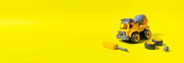 Sarı zemin üzerinde plastikten yapılmış, metin kopyalama alanı olan bir inşaat makinesi. Çarklı ve tornavidalı oyuncaklar. Detaylara ayrılabilir. Oyuncak tasarımcısı. Oyuncak mağazası için pankart.
