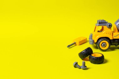 Sarı zemin üzerinde plastikten yapılmış, metin kopyalama alanı olan bir inşaat makinesi. Çarklı ve tornavidalı oyuncaklar. Detaylara ayrılabilir. Oyuncak tasarımcısı. Oyuncak mağazası için pankart.