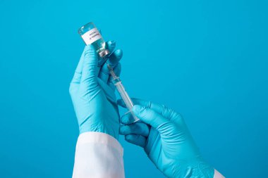 Bir doktor ya da laboratuvar teknisyeni elinde hepatit B aşısı olan bir şişe tutuyor. Mavi arkaplanda metin için bir yer