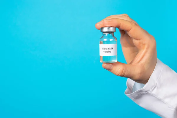 A doctor or laboratory technician holds a vial with a hepatitis B vaccine in his hand. With a place for text on a blue background