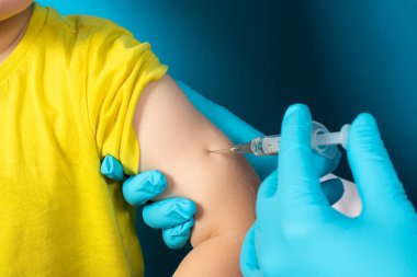 Doktor ya da hemşire mavi arka planda küçük bir çocuğa kaslı bir şırınga enjekte ediyor. Tüberküloz aşısı, BCC aşısı