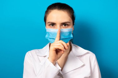 Maskeli doktor ağzında sessizlik işareti olduğunu gösteriyor. Tıp ve sağlık hizmetlerinde tıbbi gizem, tıbbi hata ve yeni tıbbi araştırmaların sırları. Tıbbi gizlilik.