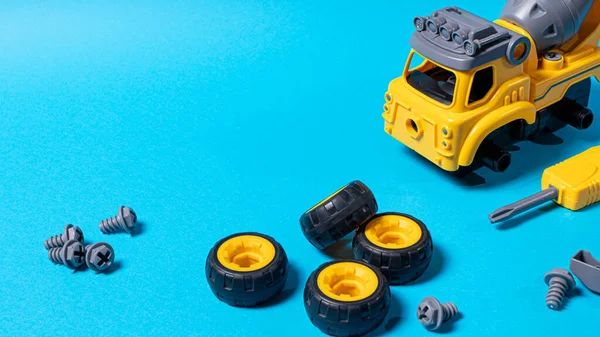 Construction yellow machine concrete mixer made of plastic on a blue background with a place for text copy space. Toy with cogs and screwdriver, which can be disassembled into details. Toy-designer. Banner for toy store.