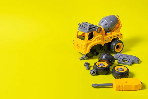 テキストコピースペースのための場所と黄色の背景にプラスチック製の建設機械コンクリートミキサー 詳細に分解することができます歯車やドライバーとおもちゃ おもちゃデザイナー おもちゃ屋のためのバナー — ストック写真