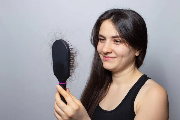 La chica sostiene un cepillo de pelo con el pelo cayendo y sonriendo. Pérdida de cabello, cuidado del cabello y tratamiento. Médico tricólogo — Foto de Stock