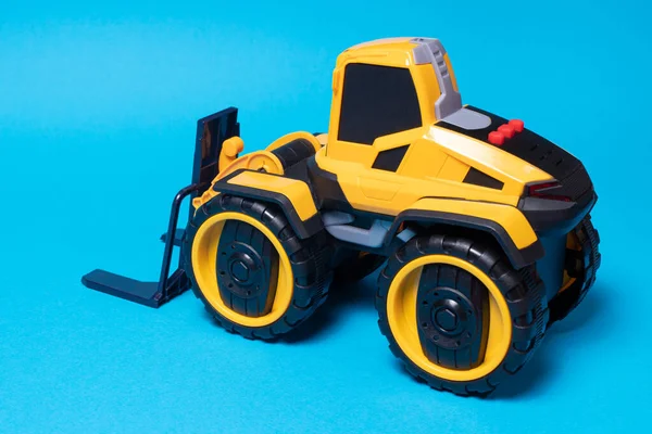 青い背景に黄色の黒いフォークリフトのおもちゃのタイプライター おもちゃ屋のための子供のための建設機械トラクター テキストのためのコピースペース — ストック写真