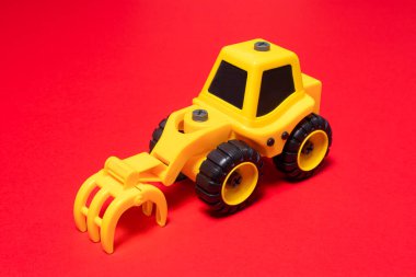 Kırmızı arka planda ormanı doldurmak için tırmık başlıklı sarı oyuncak traktörü.