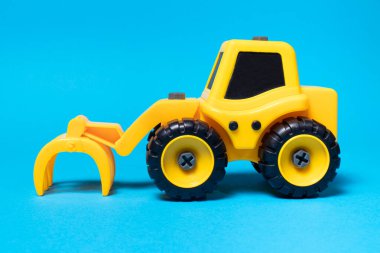 Mavi arka planda ormanı doldurmak için tırmık başlıklı sarı oyuncak traktörü.