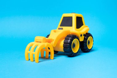 Mavi arka planda ormanı doldurmak için tırmık başlıklı sarı oyuncak traktörü.