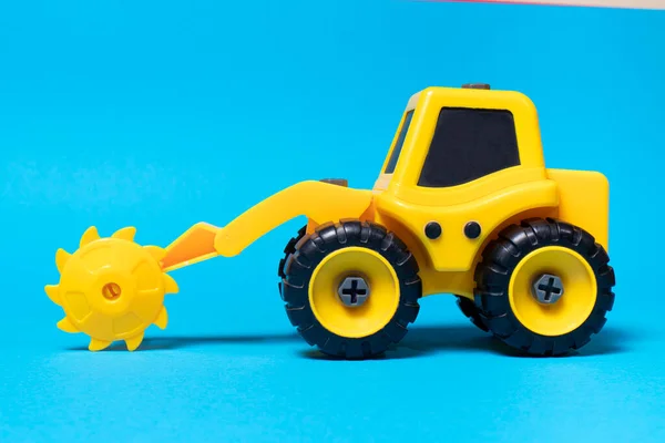 丸みを帯びたおもちゃの黄色のトラクター青の背景に木のためのノズルを見た おもちゃ屋の建設機械器具 — ストック写真