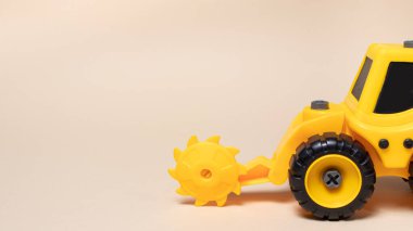 Bej ışıklı arka planda tahta için yuvarlak testereli oyuncak sarı traktör. Oyuncakçı için inşaat makinesi gereçleri.