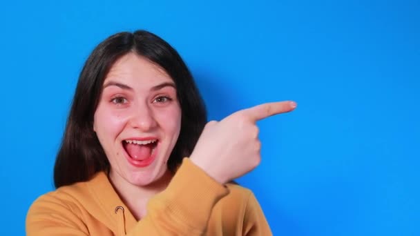 Una donna bruna mostra il dito di lato, di lato e ride, urla di gioia. Video per la pubblicità su sconti, vendite o lotterie. — Video Stock