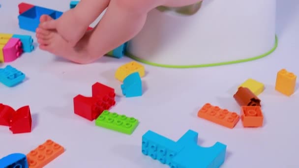 A little boy sits on a pot and plays with multi-colored designer cubes. Get used to the pot. — Stock Video