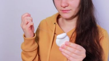 Esmer bir kadın dişlerini diş ipiyle fırçalıyor. Ağız temizliği, plağın alınması ve diş çürüğünün önlenmesi ve diş eti iltihabı. Dişçilik.