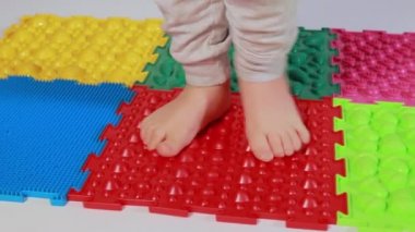 Ortopedik minderlerde küçük bir çocuğun bacakları. Yürümek ve ayağın doğru kemerini oluşturmak için parlak yüzeyler. Masaj yapboz paspası.