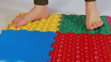 Genç bir kız ortopedik masaj minderleri üzerinde yürür, bulmacaları çözer. Düz taban ve ayak masajını önleme.