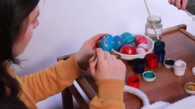 Bir kadın guaj boyalarıyla Paskalya yumurtası çiziyor. Yumurta boyamak ve Paskalya için hazırlanmak. Yumurtanın üzerinde bir tavşan resmi..