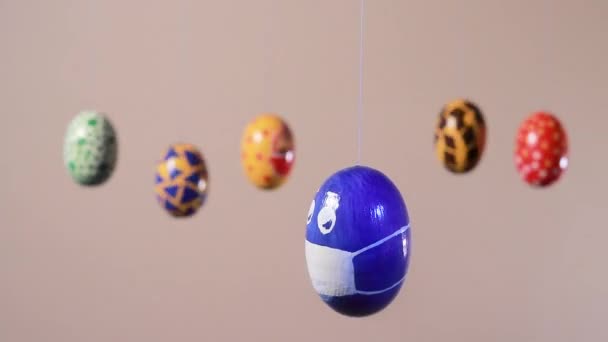 Um ovo azul com um rosto mascarado gira contra o fundo de outros ovos de Páscoa em um fundo bege claro. O conceito do coronavírus pandêmico e o feriado da Páscoa. — Vídeo de Stock