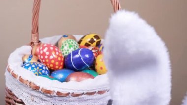 Boyanmış yumurtalarla dolu bir sepet bej renkli bir arka plana doğru kıvrılır. Ön plandaki komik tavşan kulakları büyük Paskalya avında yumurta aramak için etrafta dolanıyor. Paskalya indirimi, reklam ve satış.