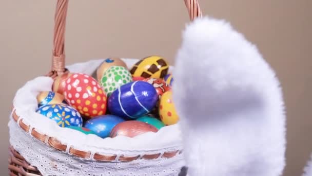 En kurv med malede æg hvirvler på en beige lys baggrund. Sjove kaninører i forgrunden går rundt og leder efter æg på den store påskejagt. Påske rabatter, reklame og salg. – Stock-video